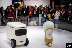 Attendees wave at Honda robotics concepts 3E-C18, left, and 3E-A18, at CES International, in Las Vegas, Nevada, Jan. 9, 2018.
