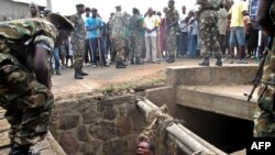 FILE - A man begs for help from the military as he stands in a drain where he had hidden to escape a lynch mob at the Cibitoke district of Burundi's capital, Bujumbura. International judges have approved the opening of a full investigation into alleged crimes against humanity in Burundi, where at least 1,200 people have died in unrest since 2015.