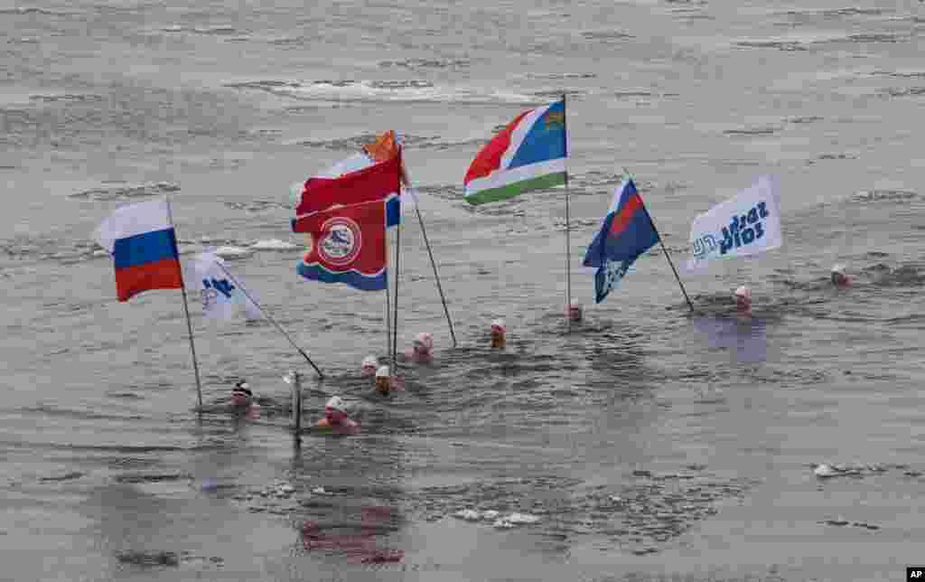 In this photo provided by Olympictorch2014.com torch bearer Alexander Brylin, with other ice swimmers, swims with Olympic torch during the torch relay in the Amur River in Blagoveshchensk, Russia's Far East.