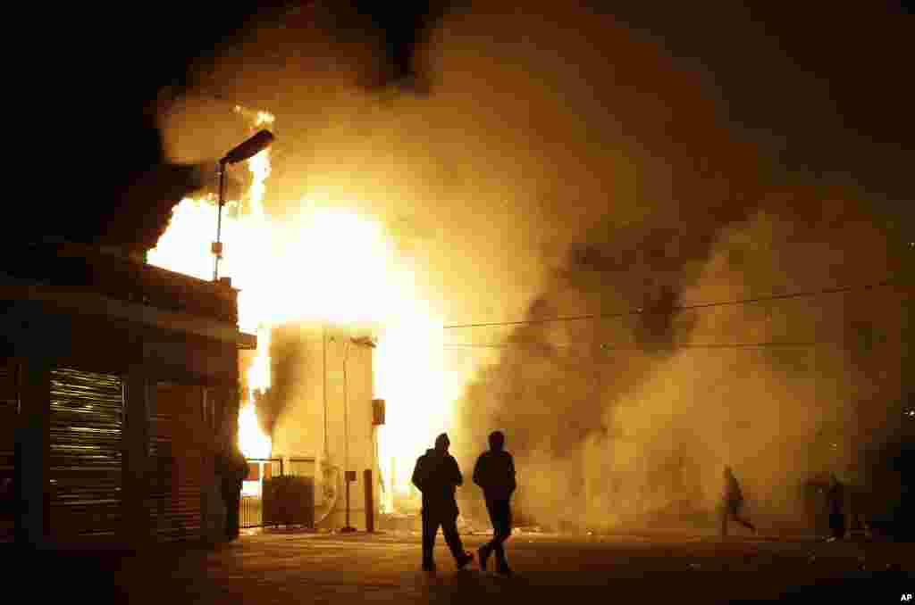 Orang-orang berjalan dekat tempat penyimpanan yang terbakar setelah pengumuman keputusan dewan juri, Ferguson, Missouri, 24 November 2014.