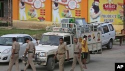 Indian policemen walk in front of a store belonging to Dera Sacha Sauda sect chief Gurmeet Ram Rahim Singh after it was sealed by authorities, near Sonipat, India, Aug. 26, 2017. Security forces on Saturday patrolled the streets of the north Indian state where mobs went on a rampage after a court declared their quasi-religious sect leader guilty of raping two of his followers. 
