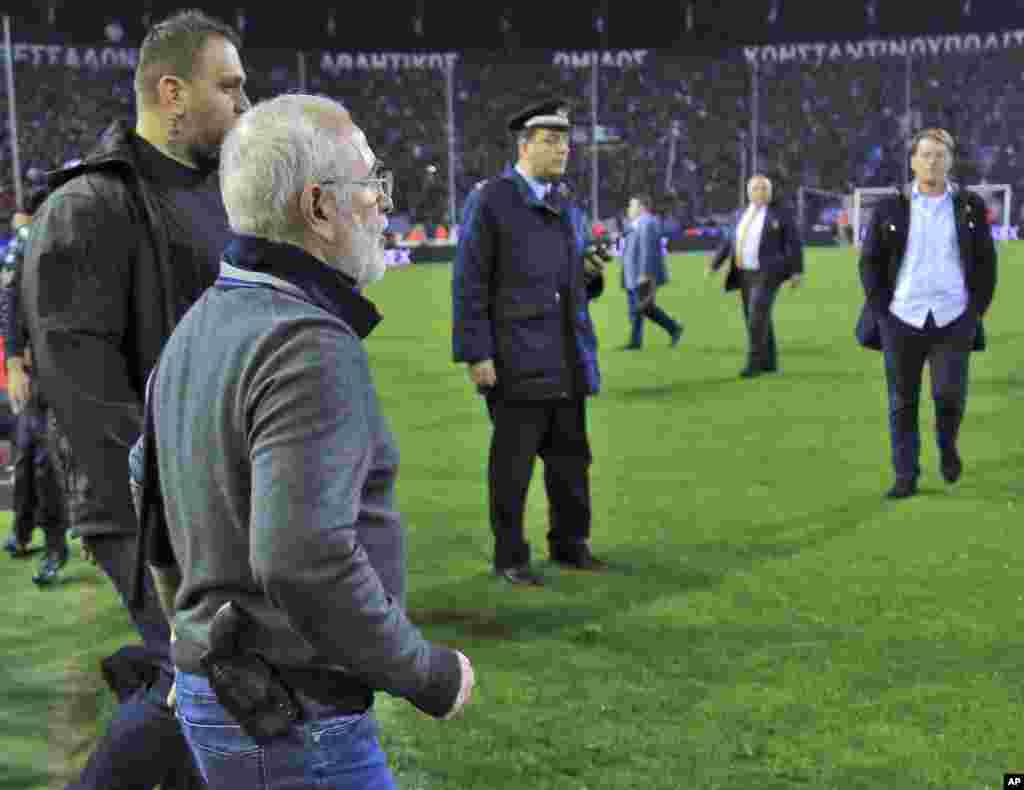 Mai kungiyar PAOK, Ivan Savvidis, rataye da bindiga a kunkuminsa, tare da masu gadinsa, a lokacin da ya kutsa cikin filin wasa a karawarsu da AEK Athens ranar lahadai a birnin Thessaloniki. Sau biyu Savvidis yana kutsawa cikin filin a lokacin wasa. Jami'an AEK sun yi zargin cewa Savvidis yayi barazana ga alkalin wasan a kutsawarsa ta farko, kafin masu gadinsa su janye shi. A karo na biyu an ga bindiga a rataye a kunkuminsa.(InTime Sports via AP)