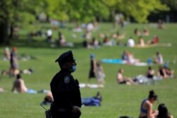 USA, New York, A New York City Police Department (NYPD) officer wearing a protective face mask watches as people gather in the Sheep Meadow in Central Park