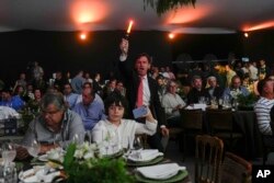 A spotter waves a light stick to signal receipt of a new bid at the Elo de Raça auction in Uberaba, Minas Gerais state, Brazil, Sunday, April 28, 2024. The Elo de Raça is the most prestigious auction at the world’s biggest Zebu fair. (AP Photo/Silvia Izquierdo)