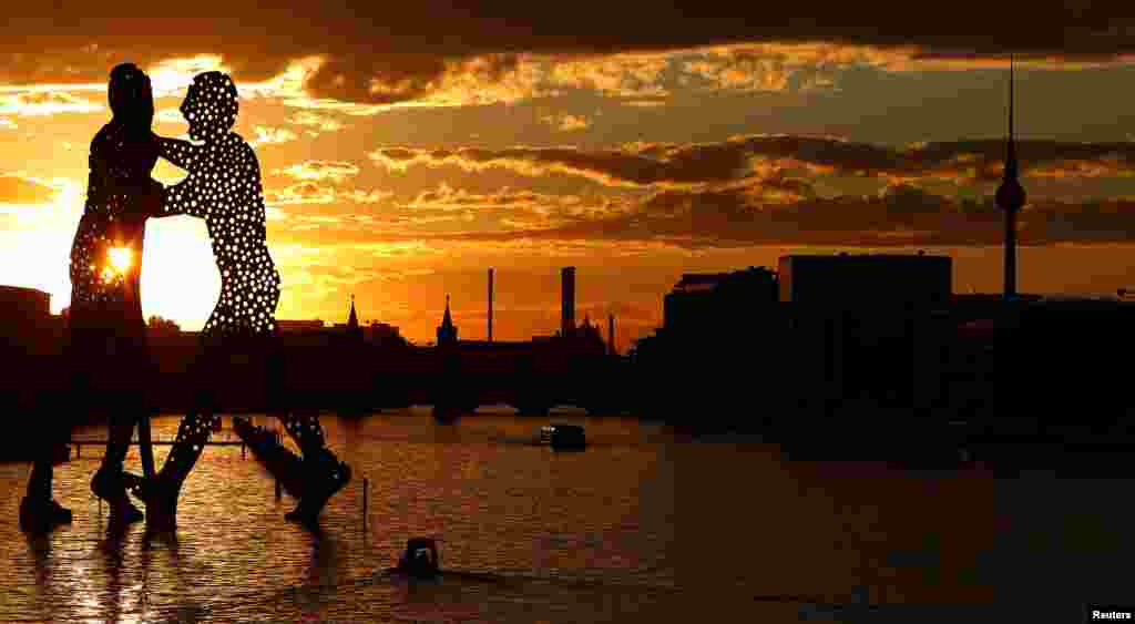 The sun sets behind the cityscape and the "Molecule Men" — a 30-meter-high sculpture by Jonathan Borofsky, located in Berlin's Spree river, Germany, Aug.7, 2016.