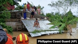 In this photo provided by the Philippine Coast Guard, residents stay on top of roofs to avoid floods while they wait to be rescued from floodwaters in Libon, Albay province, Philippines, Oct. 23, 2024. 
