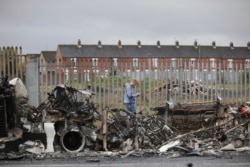 Seorang pria berjalan melewati bus yang terbakar di jalan Shankill di Belfast Barat, Irlandia Utara, Kamis, 8 April 2021. (Foto: AP)