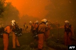 Firefighters shield themselves from embers and heavy smoke as flames close in on houses at the Sand Fire, July 23 2016, near Santa Clarita, California.