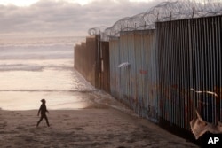 A woman walks on the beach, Jan. 9, 2019, next to the border wall topped with razor wire in Tijuana, Mexico.