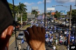 FILE - An individual watches from above as protestors march below during an anti-government protest in Managua, Nicaragua, Aug. 11, 2018.