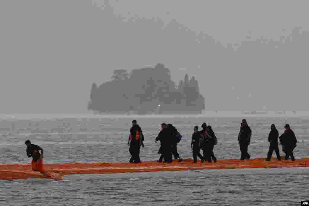 People work under heavy rain on the monumental installation "The Floating Piers" created by artists Christo and Jeanne-Claude on the lake Iseo, northern Italy. Some 200,000 floating cubes create a 3-kilometers runway connecting the village of Sulzano to the small island of Monte Isola on the Iseo Lake for a 16-day outdoor installation opening on June 18.