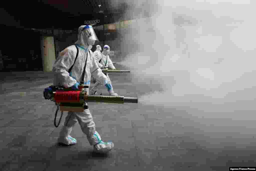 Staff members wearing personal protective equipment (PPE) spray disinfectant outside a shopping mall in Xi&#39;an in north China&#39;s Shaanxi province.