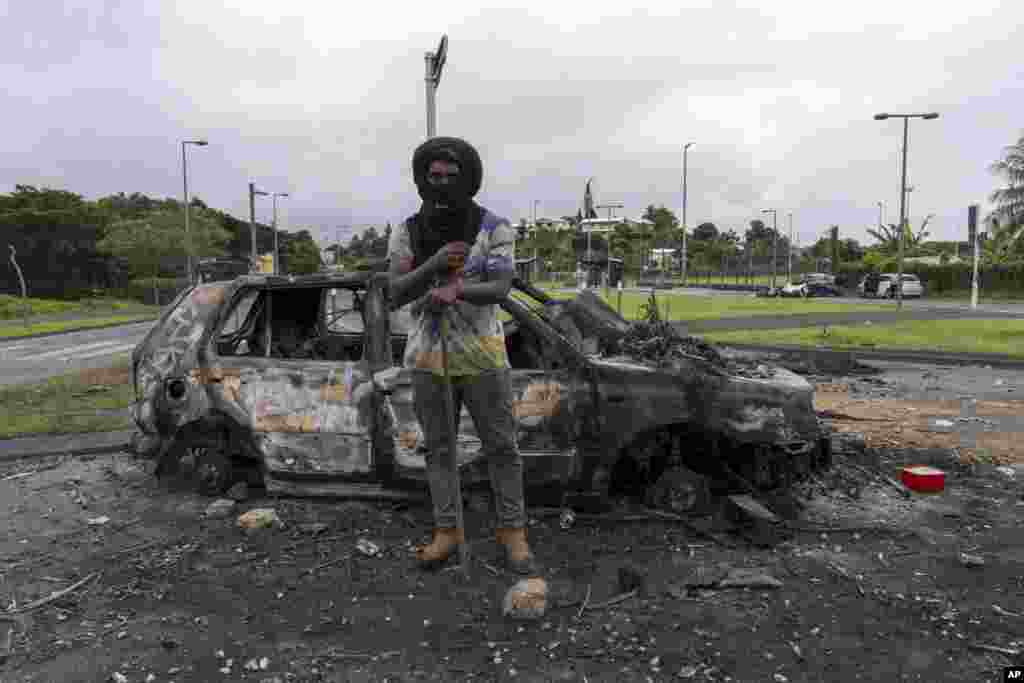 A man stands in front a burnt car after unrest in Noumea, New Caledonia, May 15, 2024.&nbsp;France has imposed a state of emergency in the Pacific territory for at least 12 days to boost security forces&#39; powers to quell deadly unrest that has left four people dead, erupting after protests over voting reforms.&nbsp;