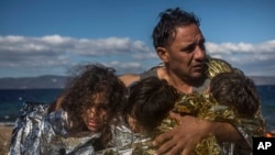FILE - A man holds three children wearing thermal blankets after their arrival in bad weather from Turkey on the Greek island of Lesbos, Oct. 28, 2015.
