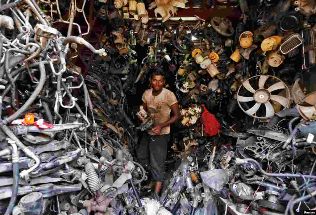A worker carries a piece from a used car inside a shop at a second-hand automobile parts market in Mumbai, India.