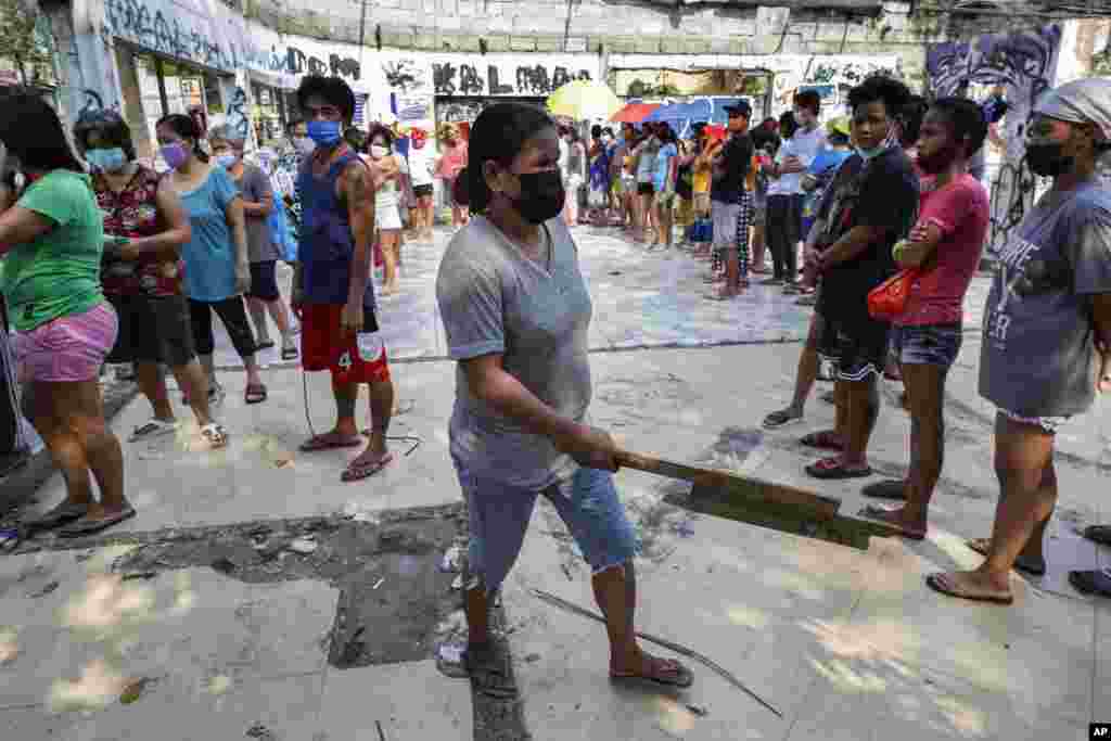 A woman holds a piece of wood as she asks other residents to maintain social distancing as they queue for free food at a &quot;community pantry&quot; which has popped up across the capital to help people cope during the government lockdown to curb the spread of the COVID-19 in&nbsp;Quezon city, Philippines.