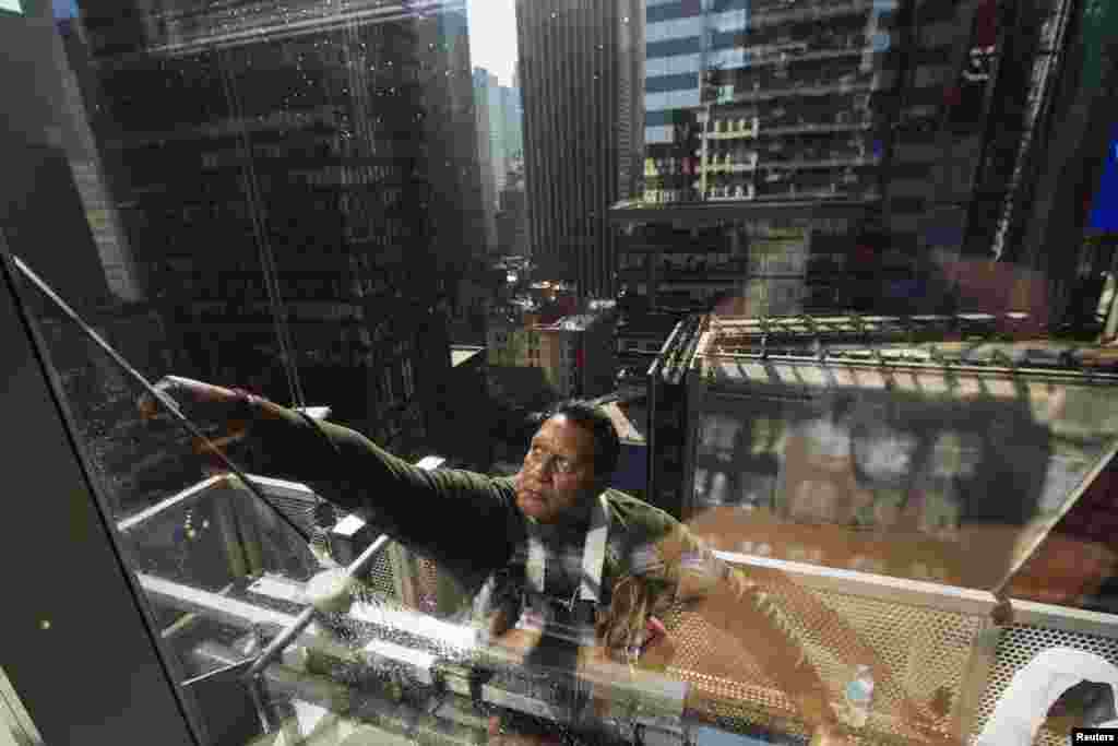 A window washer uses a squeegee to clean windows on the morning of the summer solstice in New York's Times Square.