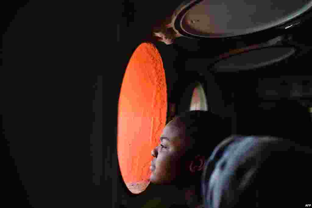 A woman looks through a window of rescue ship "Aquarius" as more the 380 migrants arrive in the port of Cagliari, Sardinia on May 26, 2016 two days after being rescued near the Libyan coasts.