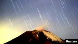 FILE - The Geminid meteor shower lights up the sky over the Mexican volcano Popocatepetl near the village of San Nicolas de los Ranchos in Puebla state, early on Dec. 14, 2004. The show for 2018 is peaking overnight on Dec. 13 and 14.