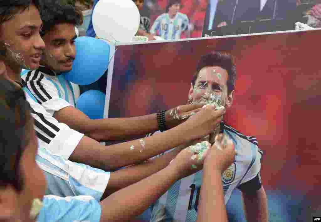 Indian football fans pose for photographers as they feed cake to a poster of Argentine striker Lionel Messi during an event to mark his birthday in Kolkata, ahead of the Copa America final where Argentina will take on Chile.