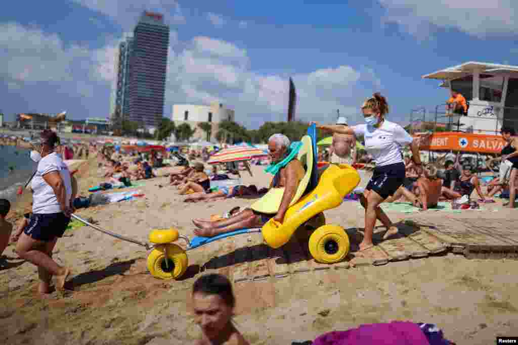 Disabled Manuel Molina, 80, sits on an amphibious chair as he is helped by lifeguards Olga Diaz and Micaela before swimming in the Mediterranean sea, on Barcelona&#39;s Nova Icaria Beach, Spain.
