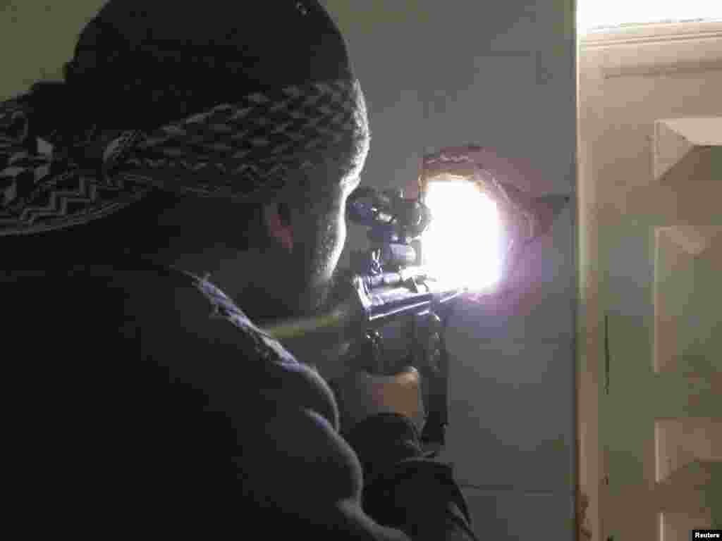A member of the Free Syrian Army points his weapon through a hole in a wall as he takes up a defense position in Daraya Feb. 4, 2013. (Shaam News Network)