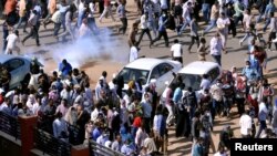 FILE - Demonstrators run from tear gas lobbed to disperse them as they march along the street during anti-government protests in Khartoum, Sudan, Dec. 25, 2018. 