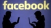FILE - Silhouettes of laptop users are seen next to a screen projection of Facebook logo in this picture illustration taken March 28, 2018. 